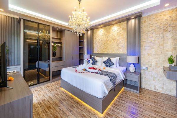 Luxurious hotel bedroom with king bed, swan towel art, rose petals, crystal chandelier, and stone accent wall.